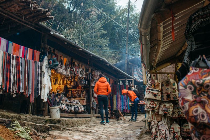 Indian tourist family walking the stone-step waterfall trail at Cat Cat Village wearing closed-toe shoes with backpacks and Vietnamese Dong cash