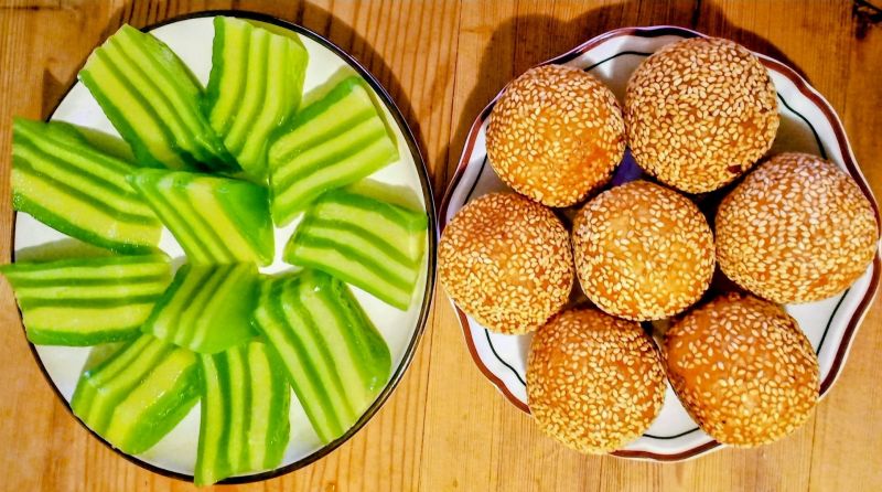 Vietnamese Banh Da Lon green-and-yellow pandan layer cake slices and Banh Cam fried sesame-coated mung bean balls plated together at a street stall