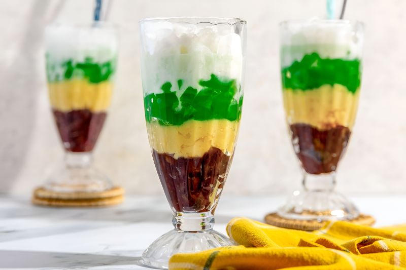 Che Ba Mau Vietnamese three-color dessert in a tall glass with visible pandan jelly, yellow mung bean paste, red kidney beans and coconut cream topped with crushed ice
