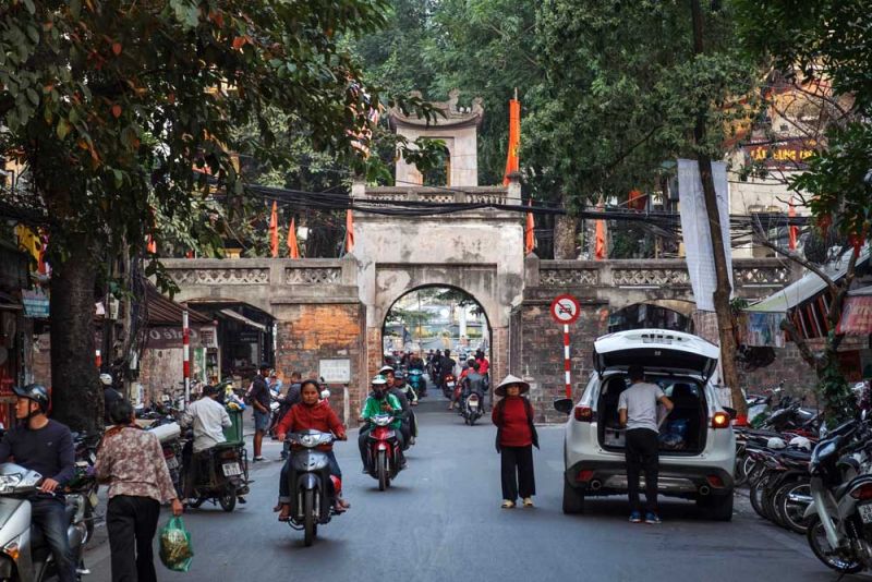 Narrow tube houses and motorbikes lining a guild street in Hanoi Old Quarter, with vendors and shop signs visible