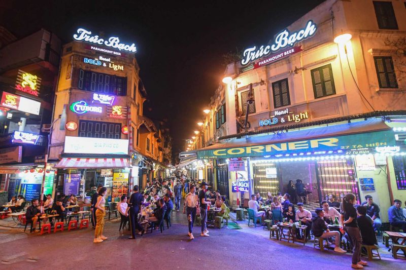 Hanoi Old Quarter nightlife scene on Ta Hien Beer Street showing plastic red stools, bia hơi vendors, hanging lanterns, and crowds of tourists