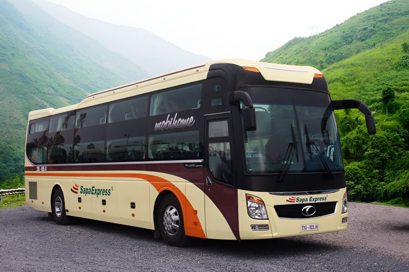 Sapa Express branded sleeper bus in cream and maroon livery parked on a green mountain road in northern Vietnam