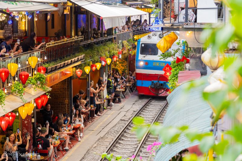 Hanoi Train Street evening train passing between Phung Hung cafes with red lanterns and second-floor terrace seating