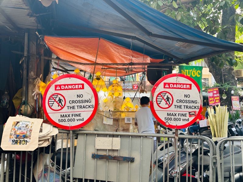 Hanoi Train Street danger warning signs at Phung Hung entrance barrier with no crossing and 500000 VND fine notice