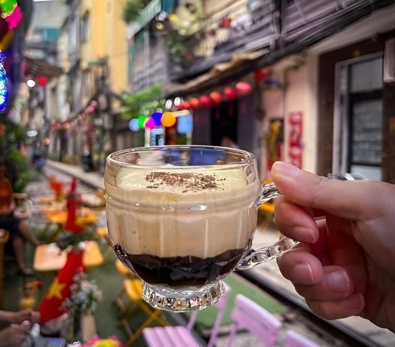 Active train passing within centimetres of café tables and house walls on Hanoi Train Street on Phung Hung Street