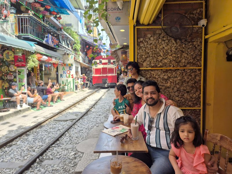 Indian family with children at Hanoi Train Street Phung Hung cafe with iced coffee and approaching train in background