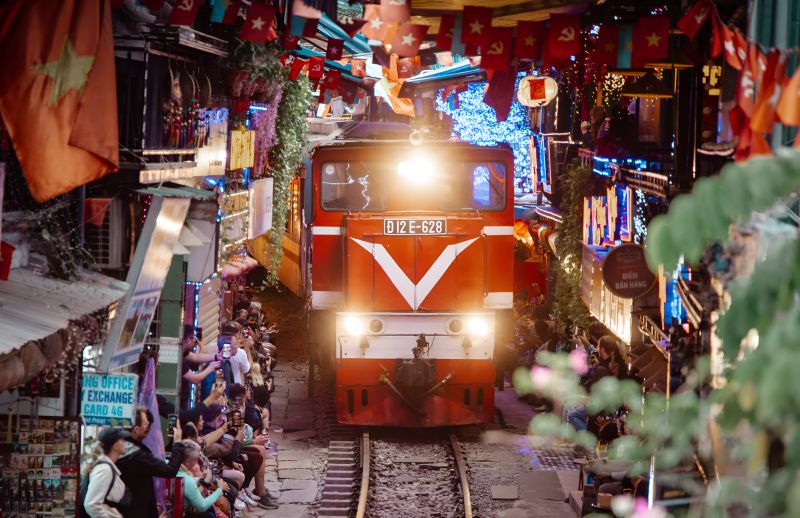 Hanoi Train Street night train passing through narrow lane with visitors seated less than one metre from the locomotive