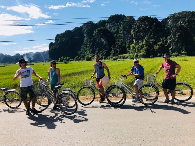 Cyclists on the Hoa Lu Ancient Capital cycling route passing rice paddies and karst limestone hills in Ninh Binh