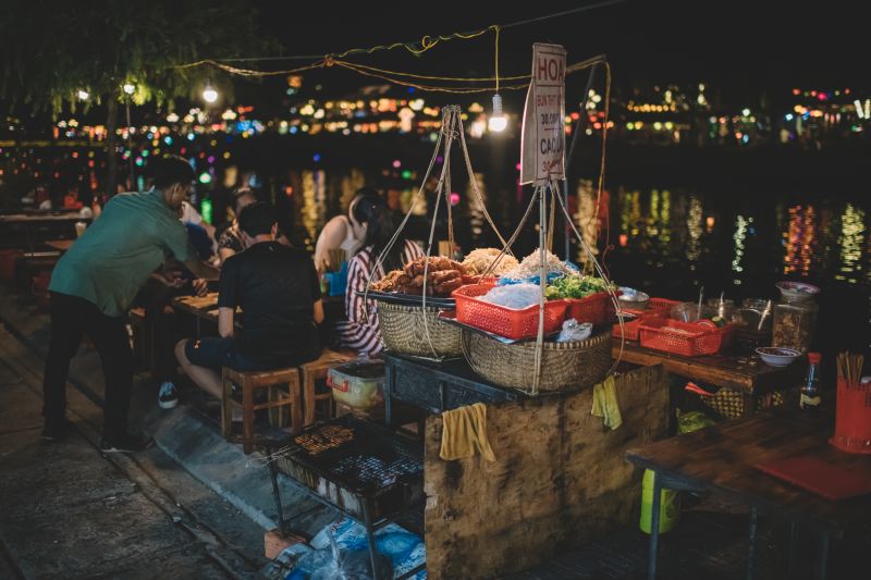 Food stalls at Hoi An Night Market with riverside diners enjoying Cao Lau and Banh Vac