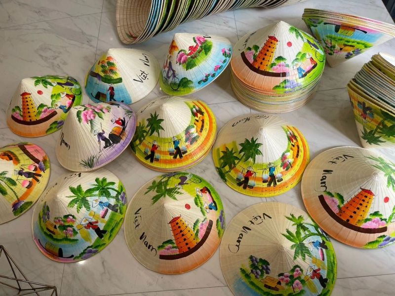 Collection of hand painted Non La conical hats on marble surface with Vietnam countryside scenes palm trees and traditional figures in bright colours