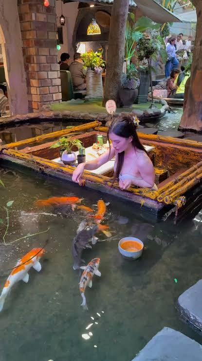 Family feeding koi fish from a pond-side table at Oasis Cafe, Ho Chi Minh City