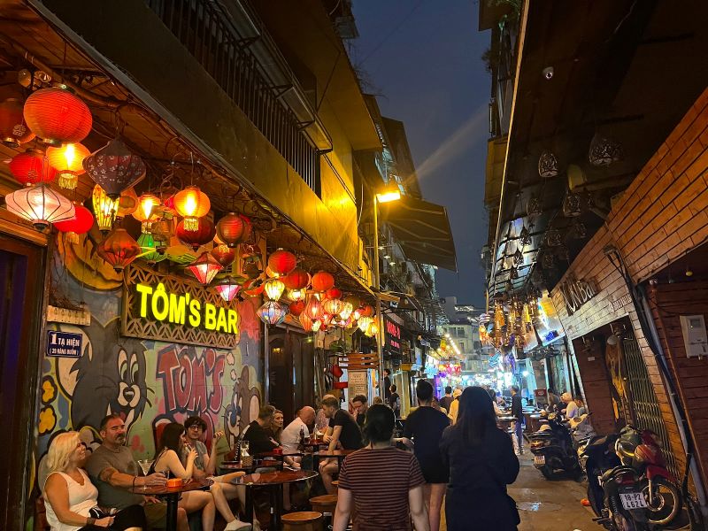 Ta Hien Street nightlife scene at night with open-air bia hoi stalls, standing bars, and crowds in Hanoi Old Quarter