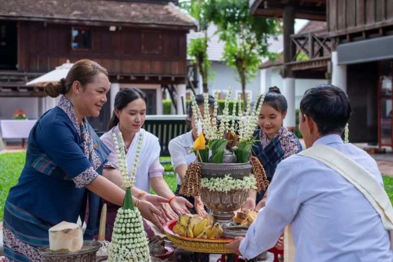 Baci ceremony in Laos with a pha khwan silver centrepiece arranged with marigolds and white sai sin cotton strings being tied around a guest's wrist