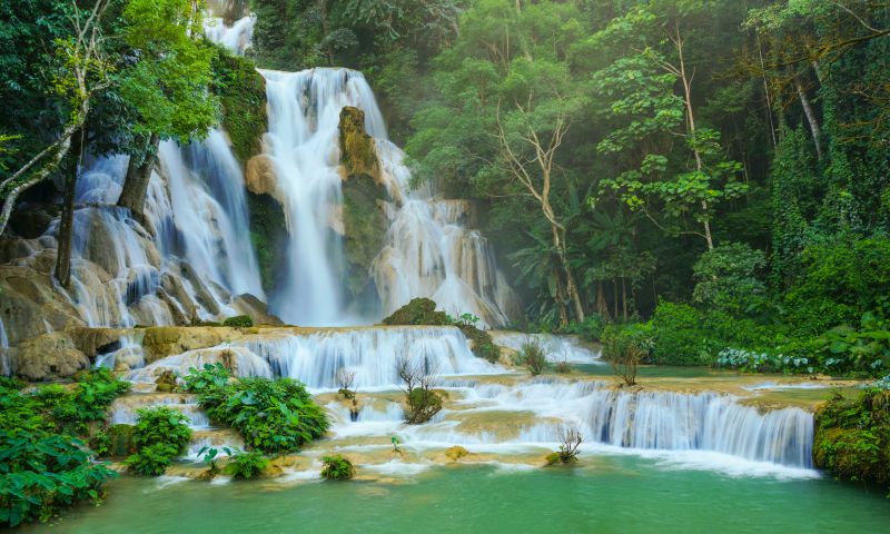 Turquoise-blue tiered limestone pools of Kuang Si Waterfalls in Laos surrounded by tropical forest