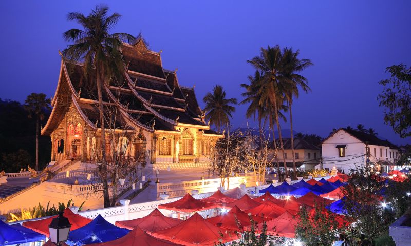 Luang Prabang Night Market in Laos with rows of red canopy stalls selling Hmong textiles silk scarves and handmade lanterns at dusk