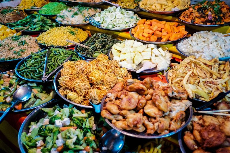 Plates of traditional Lao street food including Laap salad sticky rice in bamboo basket and grilled Ping Kai chicken at a Luang Prabang night market stall