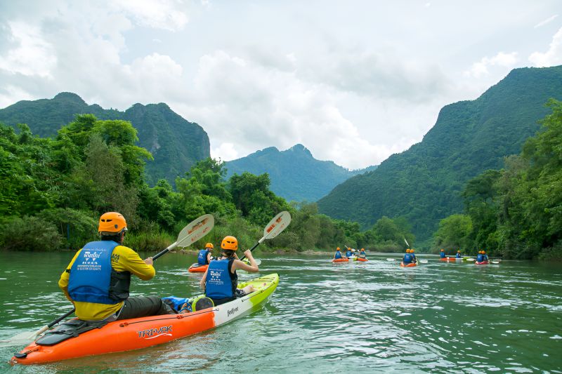 Kayakers paddling on the Nam Song River in Vang Vieng Laos against a backdrop of vertical limestone karst mountains
