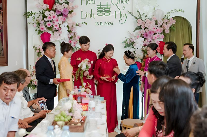 Traditional Vietnamese wedding attire — bride in red embroidered Ao Dai with phoenix motif and groom in Áo Gấm brocade robe with Khăn Xếp silk turban