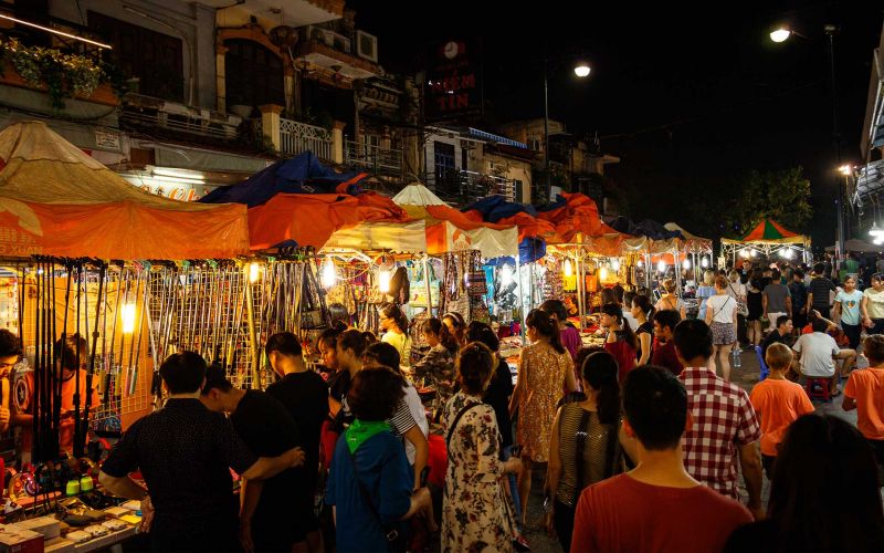 Crowded Vietnam night market street with orange and blue canopy stalls selling handicrafts and accessories under warm lighting