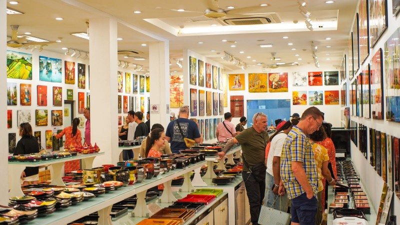 Vietnamese lacquerware shop interior with glossy bowls trays and plates on glass shelves and colourful paintings on white walls with tourists browsing