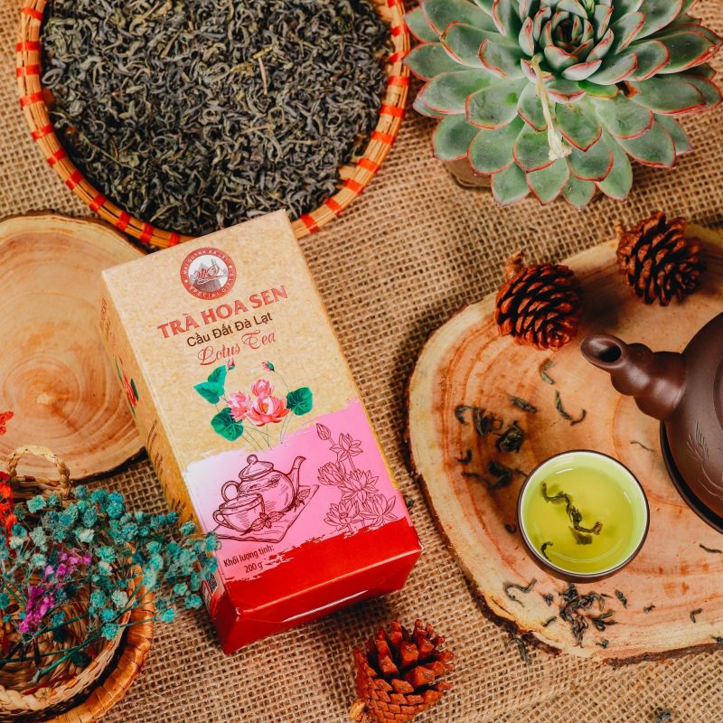 Tra Hoa Sen lotus tea pink and cream gift box beside bamboo tray of loose green tea leaves clay teapot and brewed green tea cup