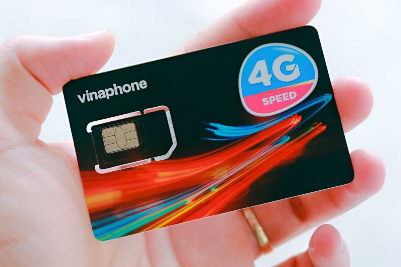Hand holding a black Vinaphone 4G Speed prepaid SIM card with colorful light streak design and nano SIM chip visible